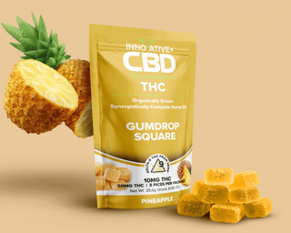 CBD THC Gumdrop Square packaging with pineapple and gummies on a beige background