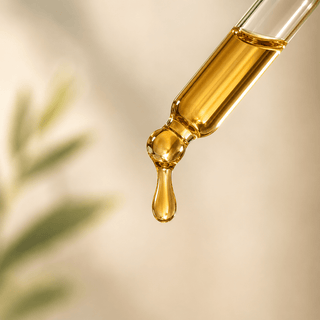 Close-up macro of golden broad spectrum CBD oil droplet in glass dropper with soft neutral wellness background