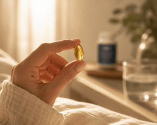 Hand holding a golden enteric CBD softgel capsule in warm natural light with a calming luxury wellness lifestyle setting.
