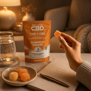 Lifestyle image of Innovative CBD Tangerine THC and CBD Gumdrop Squares in a warm evening wellness setting with sparkling water, journal, and hand holding a gumdrop.