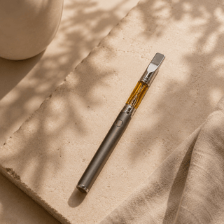 Innovative CBD whole-plant vape cartridge attached to a matte battery resting on a natural stone surface in a minimalist luxury wellness setting with warm natural lighting.